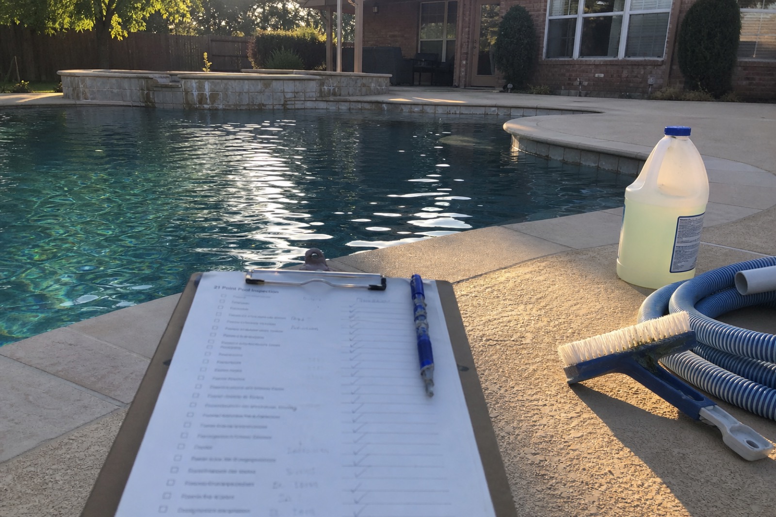 21-point pool inspection clipboard with handwritten checkmarks resting on the edge of a residential pool, late afternoon.